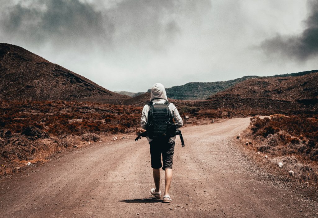 A man carrying a backpack walking on a dusty road.