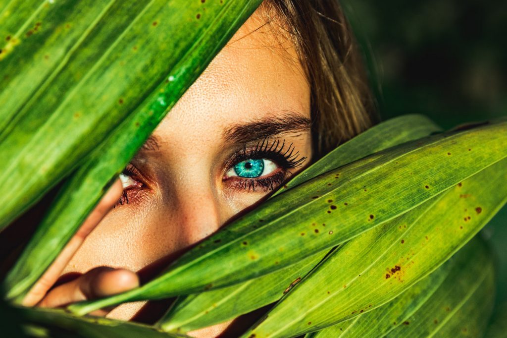 A woman hiding behind green leaves.