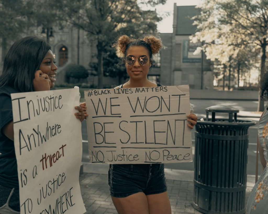 Two black women holding protesting signs with black lives matter messages.