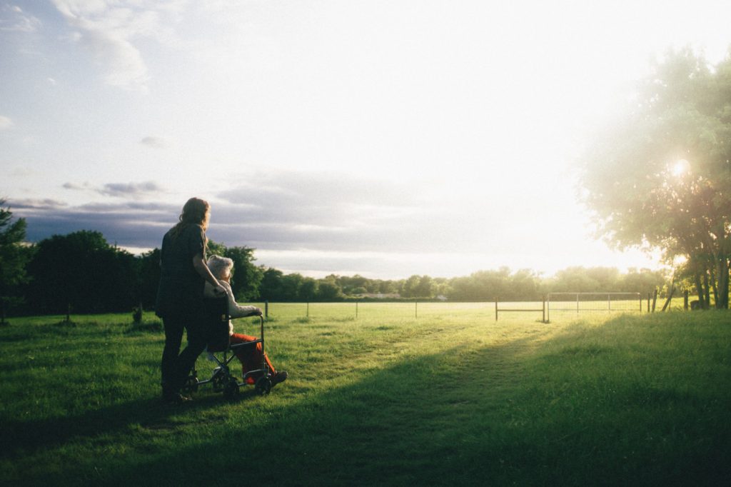 A woman pushing an old lady in a wheelchair on a green field.