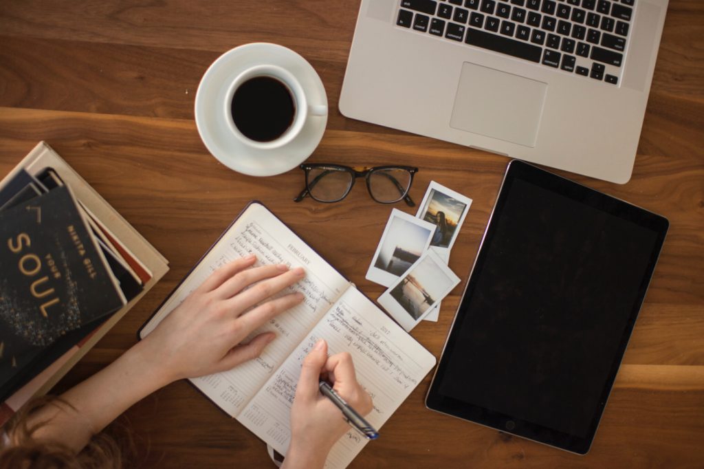 A person writing in a notebook, and a powered off tablet nearby.