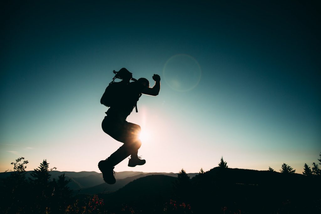 A silhouette of a person jumping on a hill.