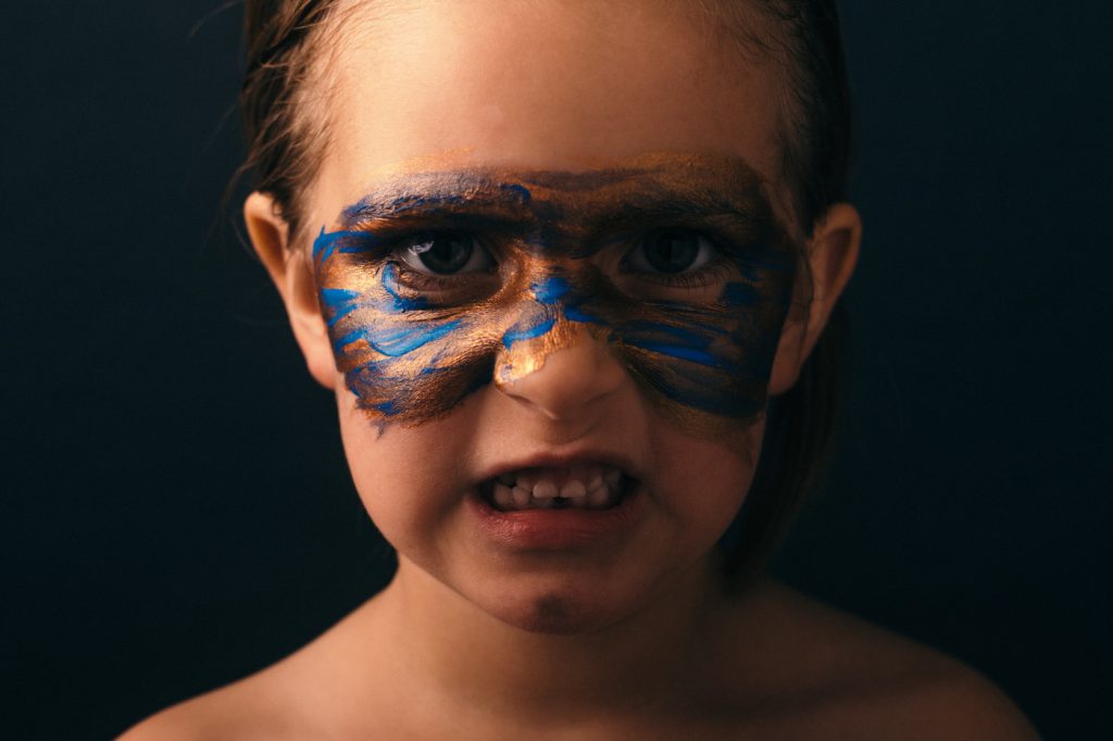 A girl wearing a face paint portrait, showing teeth.
