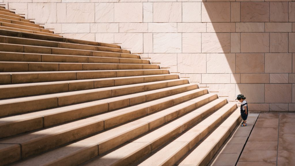 A toddler's standing in front of a concrete staircase.