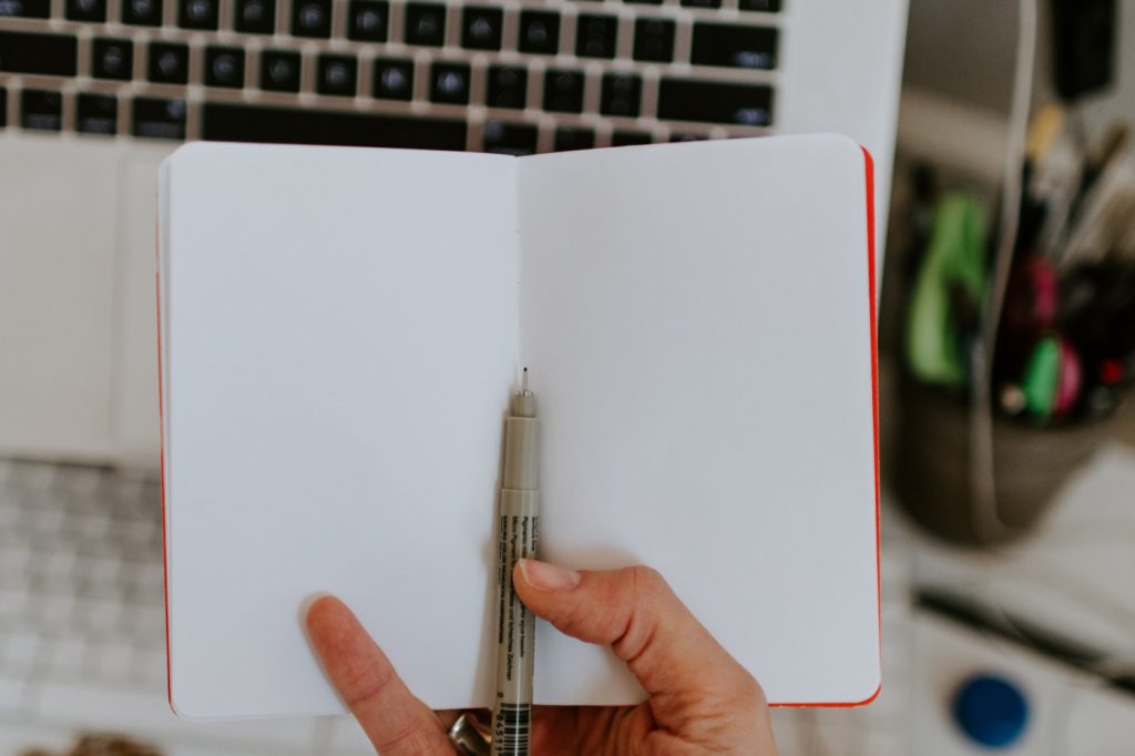 A person holding an empty notebook and a pen.
