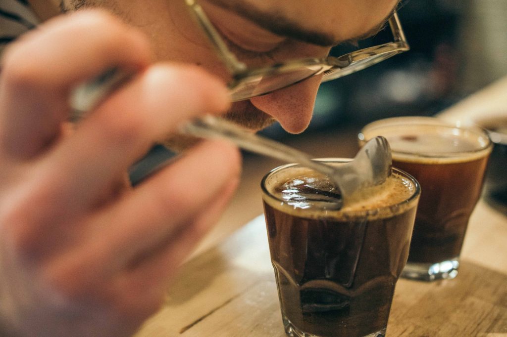 A person examining coffee with a spoon.