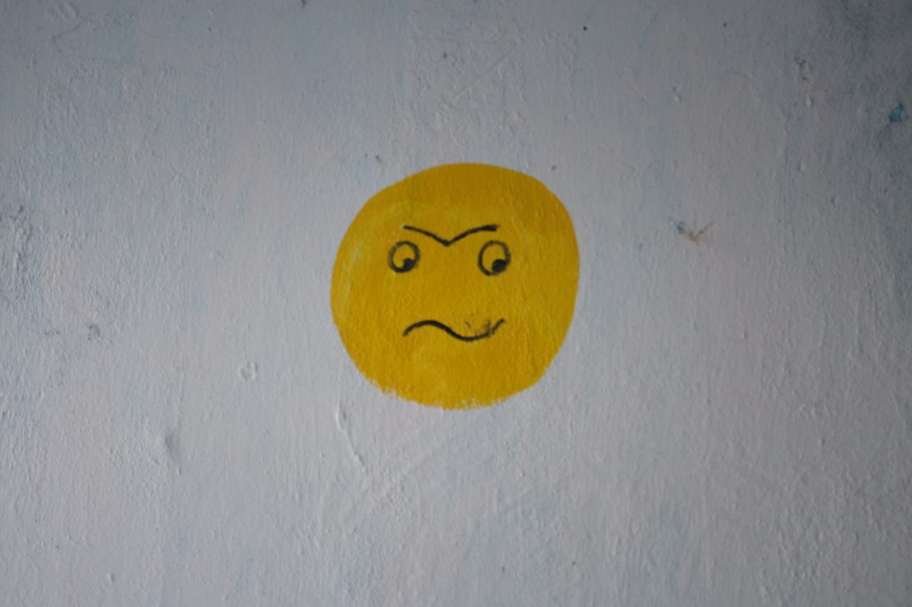 A yellow painting of an angry face resembling an emoji.