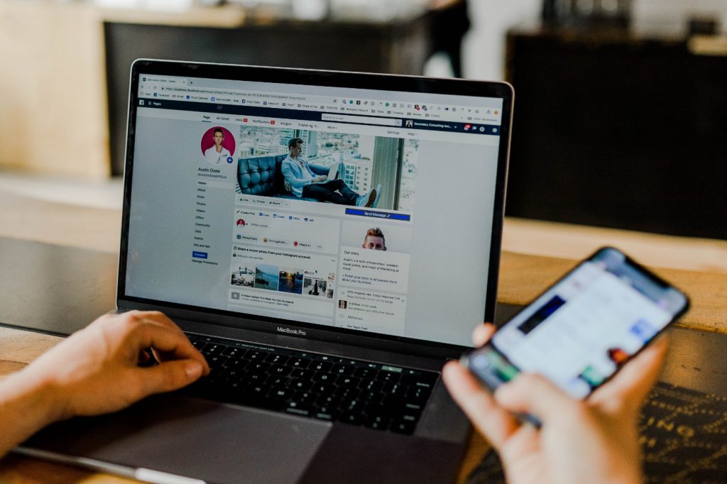 A person using both laptop and smartphone with a social media network open on each.