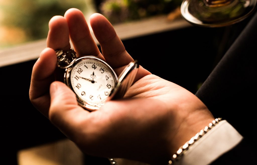 A person holding a silver-colored pocket watch.