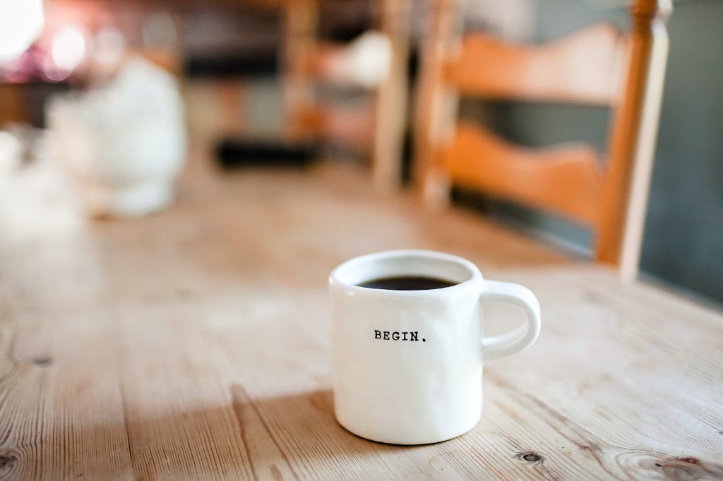 A cup of coffee on a desk with the word "begin" written on it.