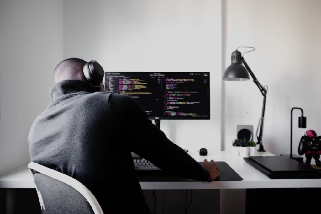 A worried person holding their head sitting on a chair in front of a computer with a code editor opened.