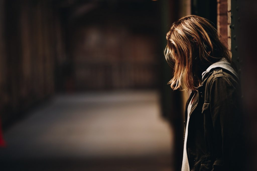 A disappointed woman leaning against a wall in a dim hallway.