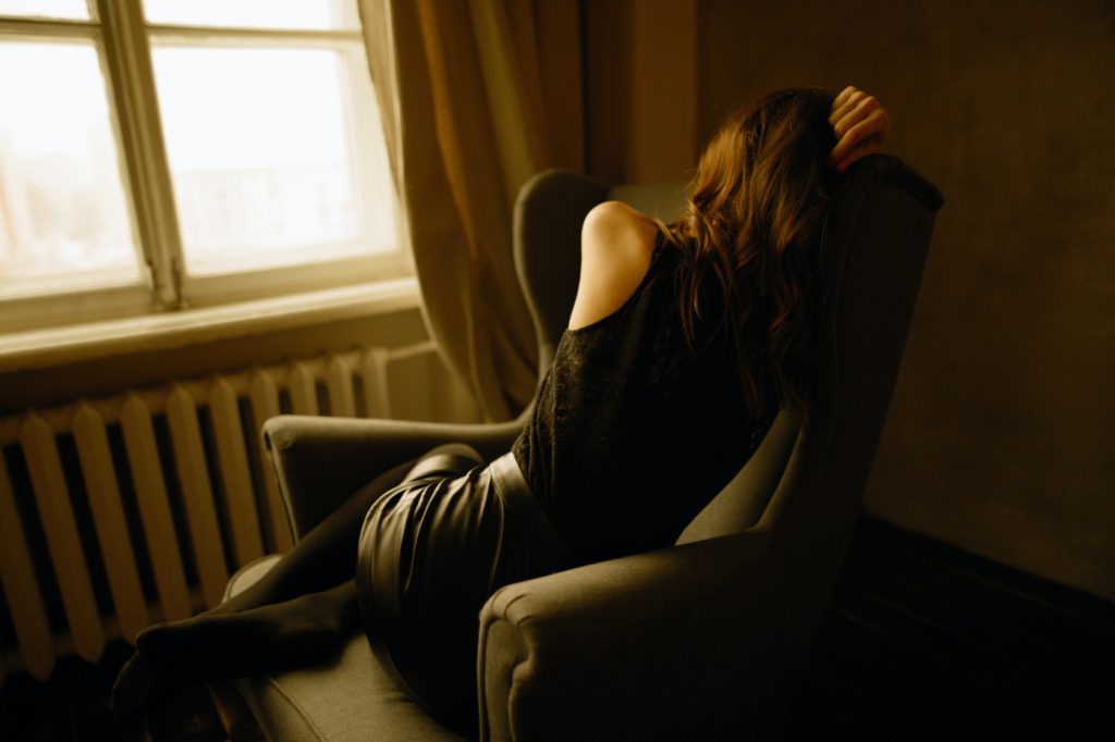 A depressed woman sitting on a chair holding her head.