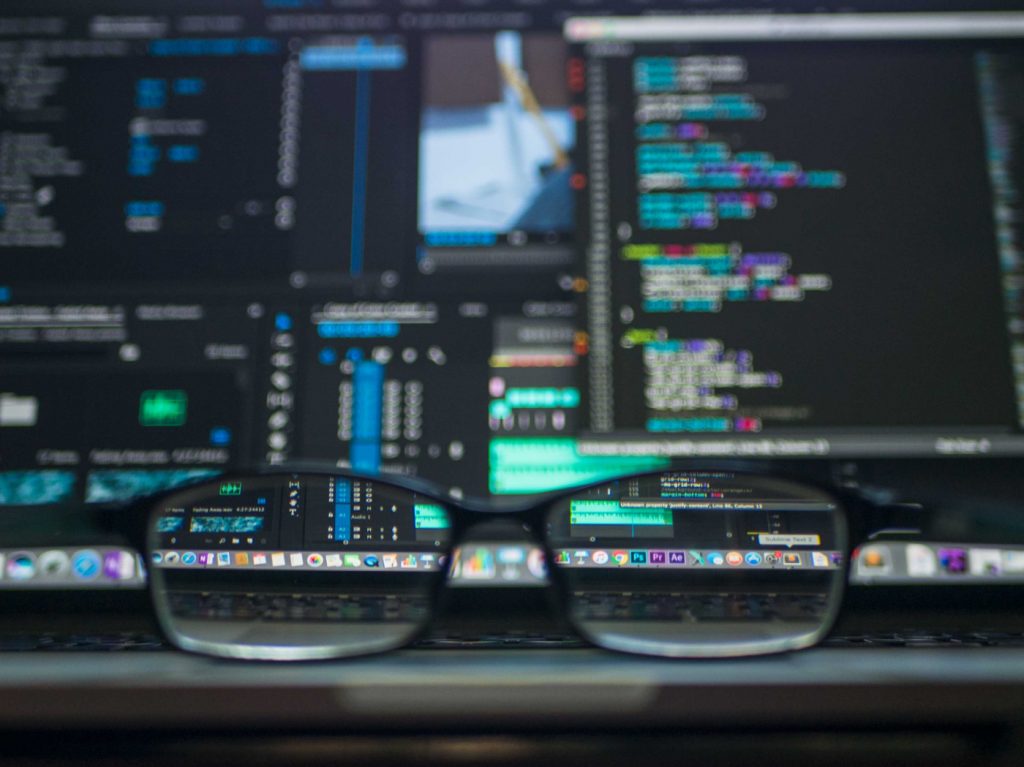 Glasses on a desk in front of a laptop with an opened code editor.