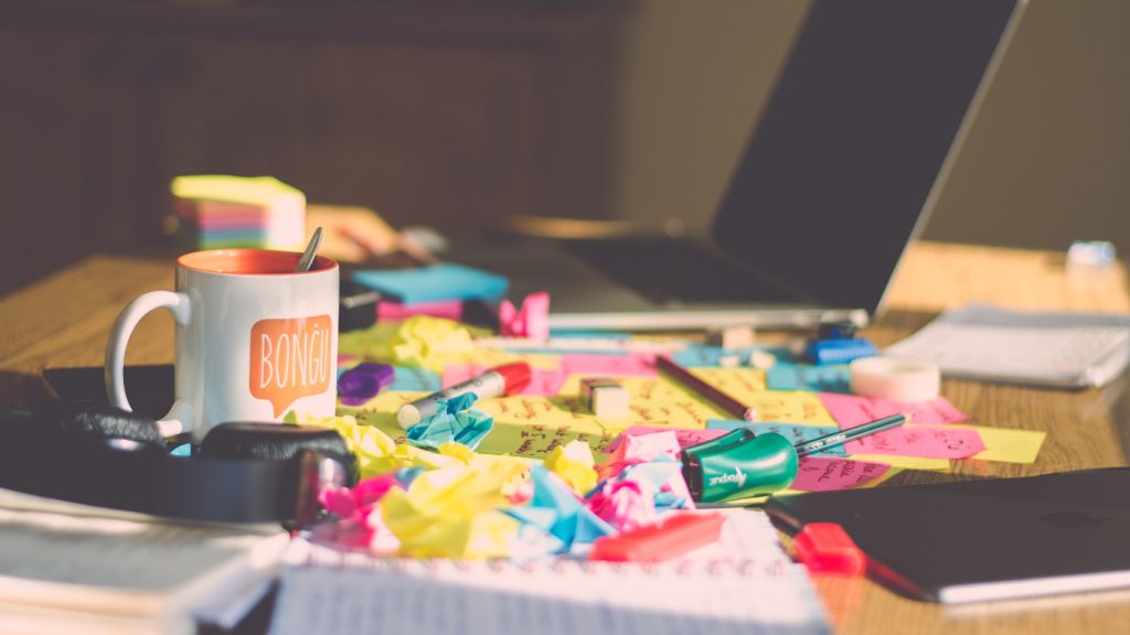 A messy desk with countless sticky notes and random accessories beside an open laptop.