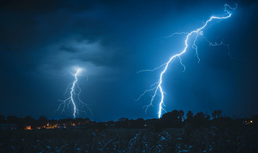 Two bolts of lightning simultaneously striking a forest during nighttime.