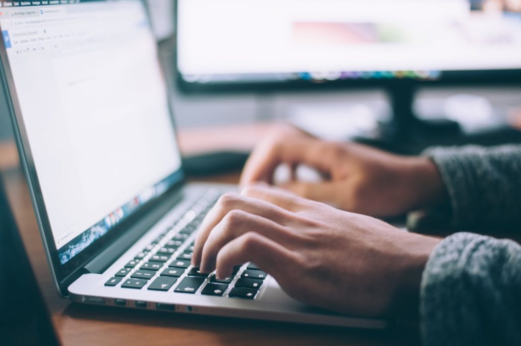 A person in front of an open laptop with an opened word processing application on the screen.