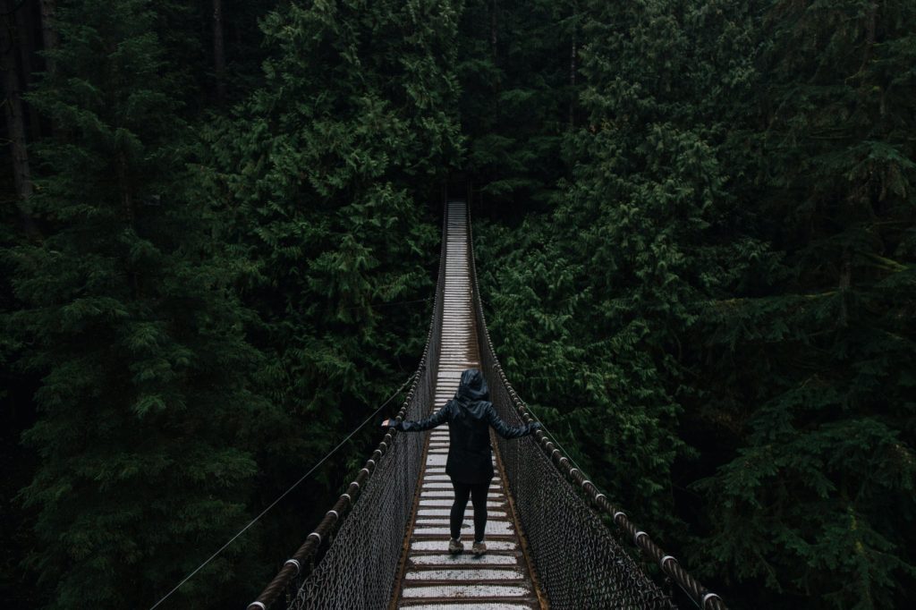 A woman walking across a suspension bridge.