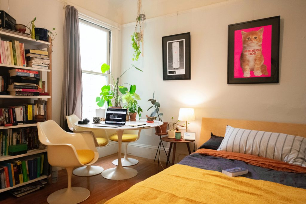 A desk with an opened laptop next to a bed in a cozy bedroom.