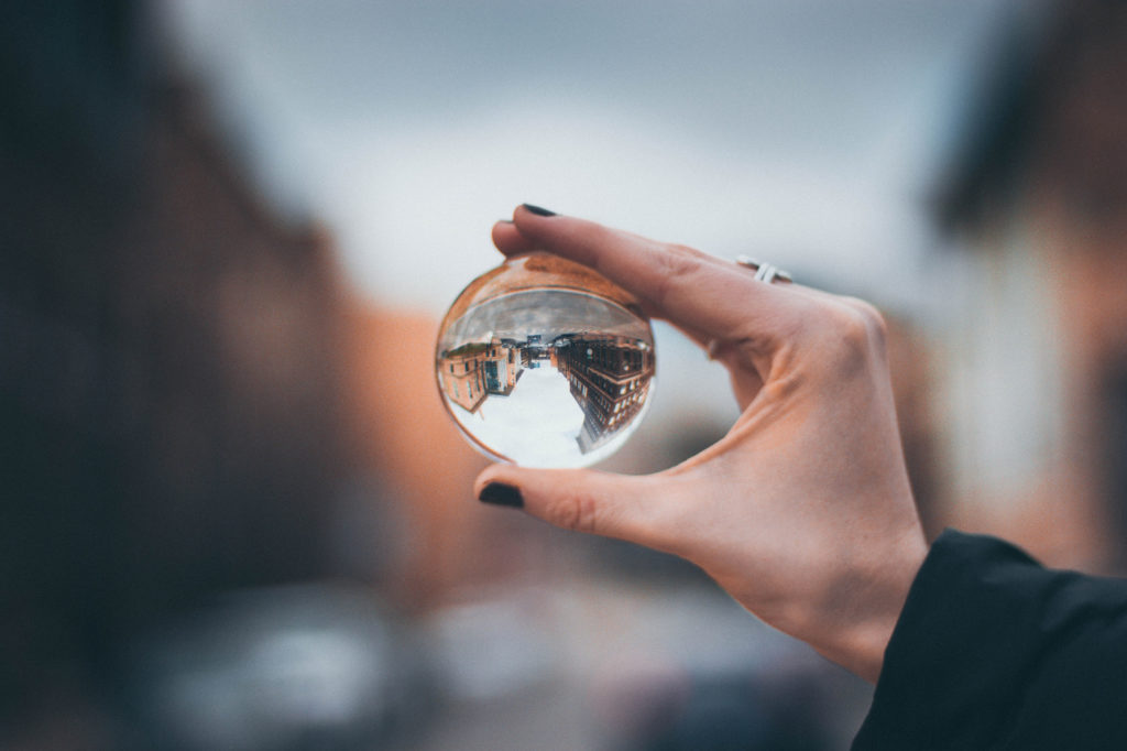 A person holding a clear glass ball through which everything looks upside-down.