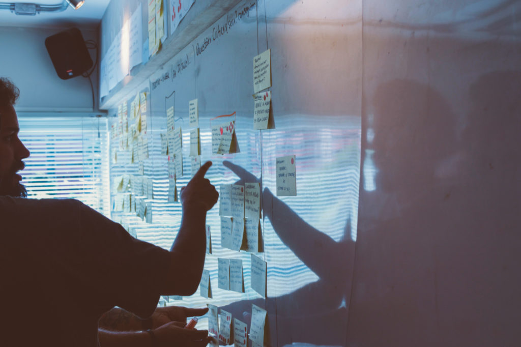 A person pointing to one of the numerous sticky notes on a whiteboard.