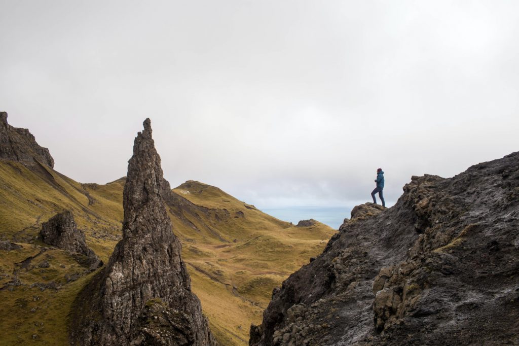 A person standing on top of a rock formation, advancing towards an even higher peak.