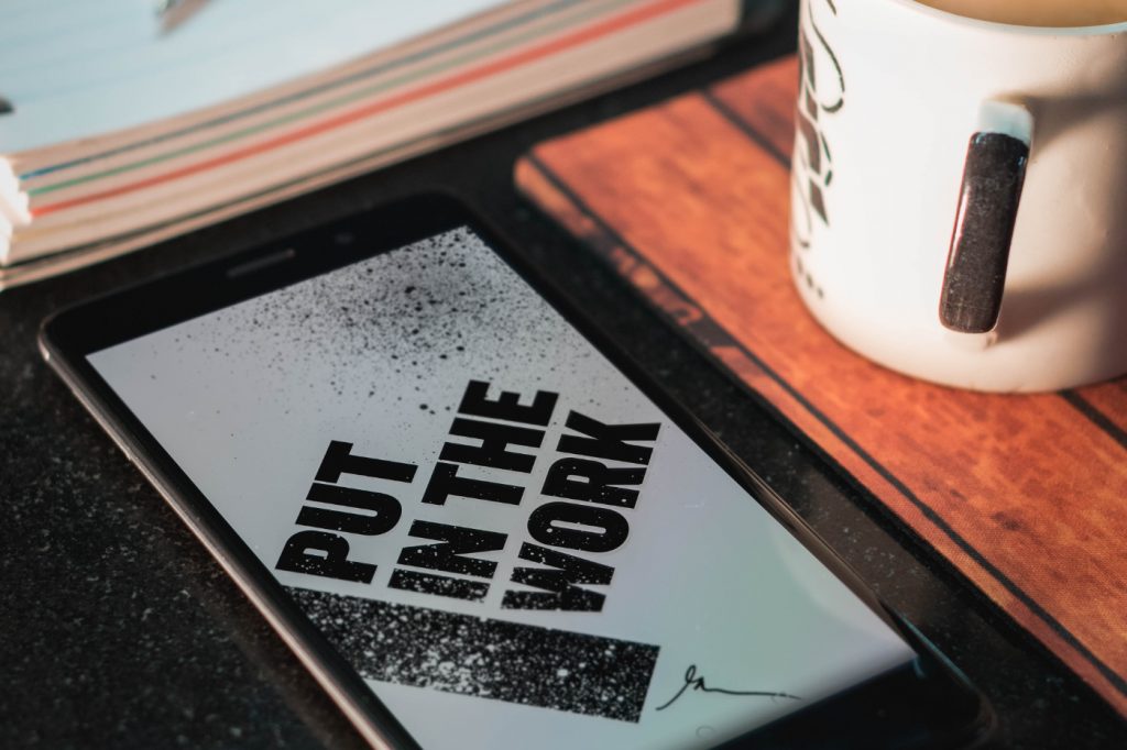 A smartphone on a desk with "put in the work" written on the screen.