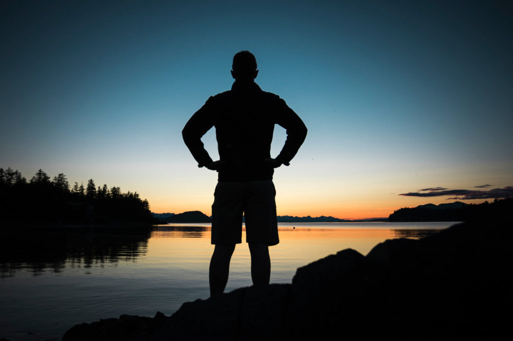 A person standing by a lake in a superhero pose.