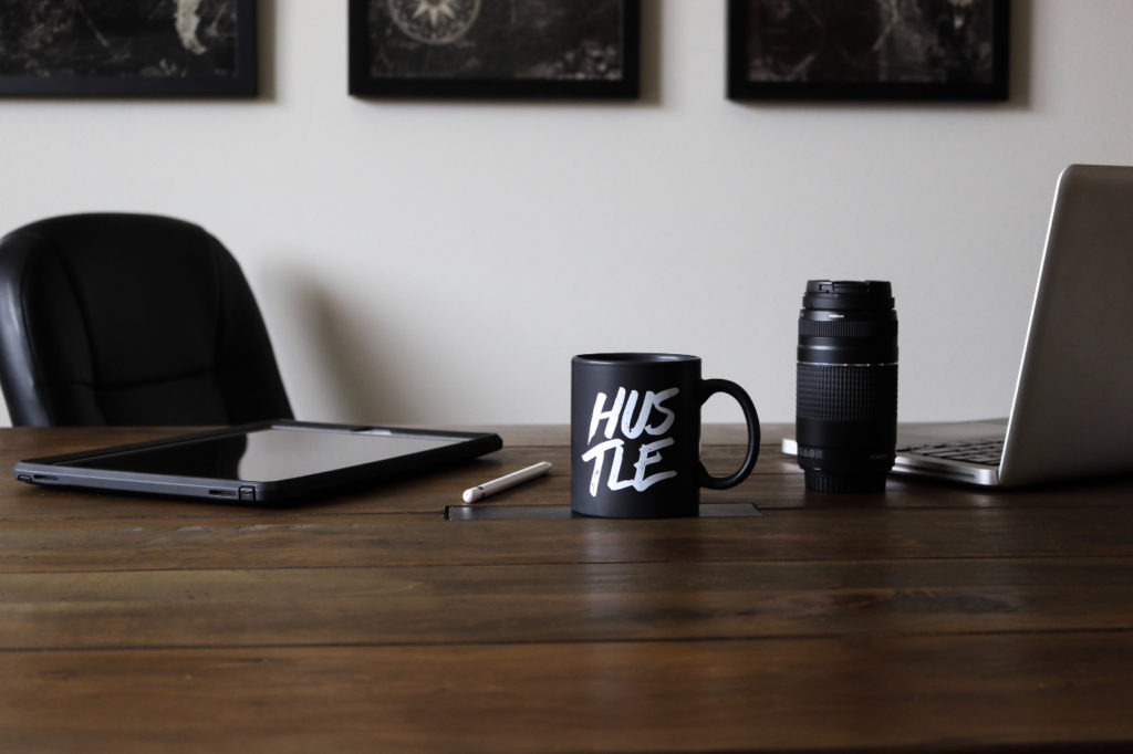 A mug on a desk next to an open laptop with the word "hustle" written on it.