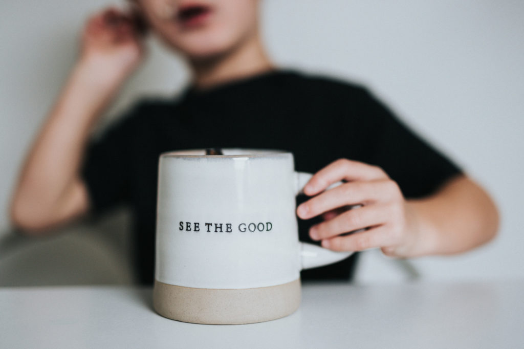 A person holding a mug with "see the good" written on it.