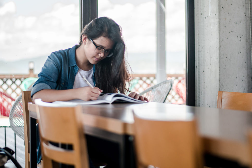 A person reading a book and taking notes at a desk.