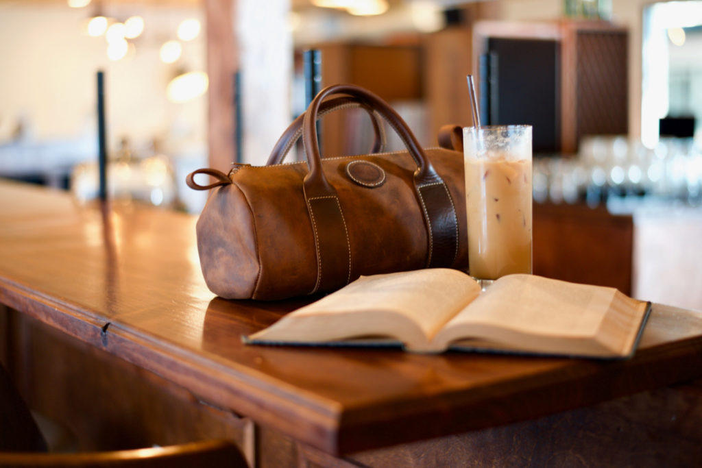 A bag on a desk next to an opened book.