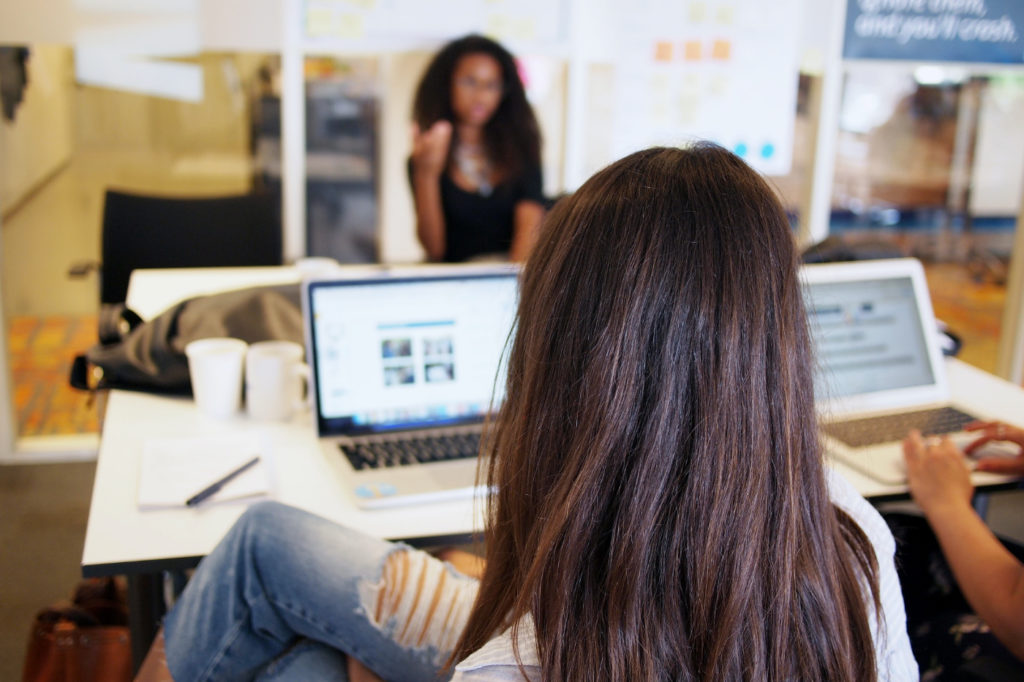 Two people in a discussion in an office behind laptops.