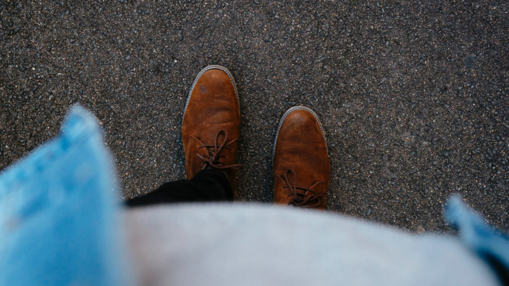 A person standing on a street, looking at their own feet.