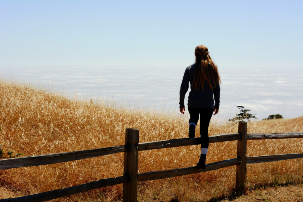 A woman stepping over a wooden fence in a field.