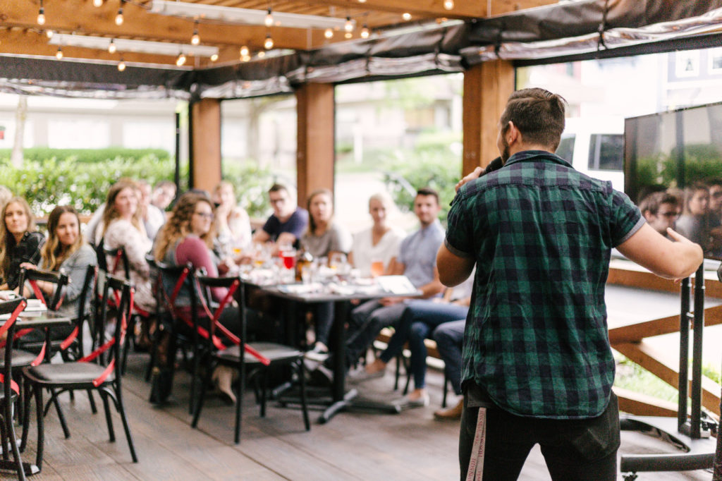 A person with a microphone speaking in front of a small group of people.