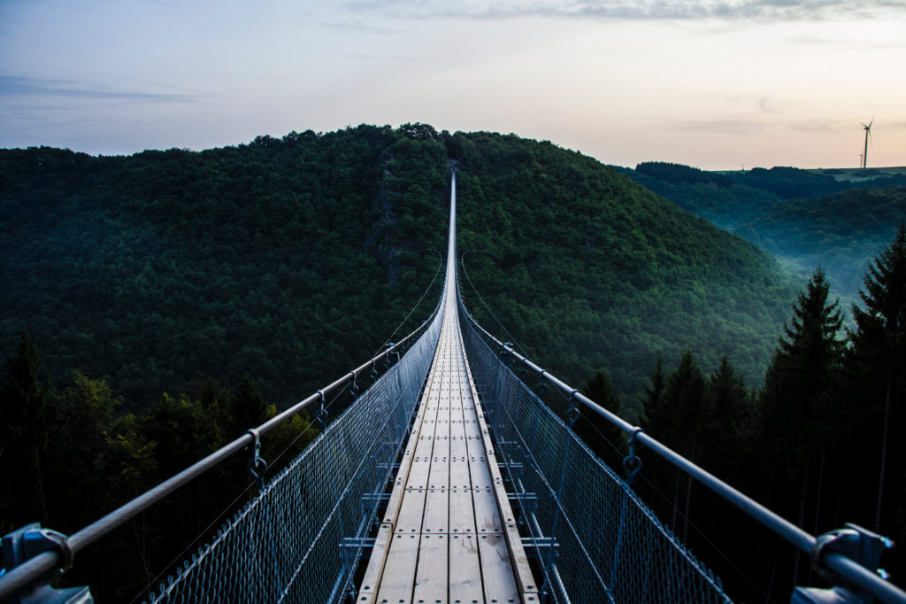 An incredibly long hanging bridge across mountains covered by trees.