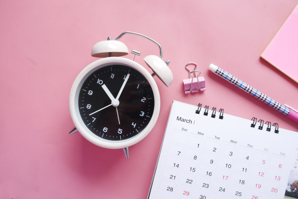 A clock, a calendar, and a pen on a desk.