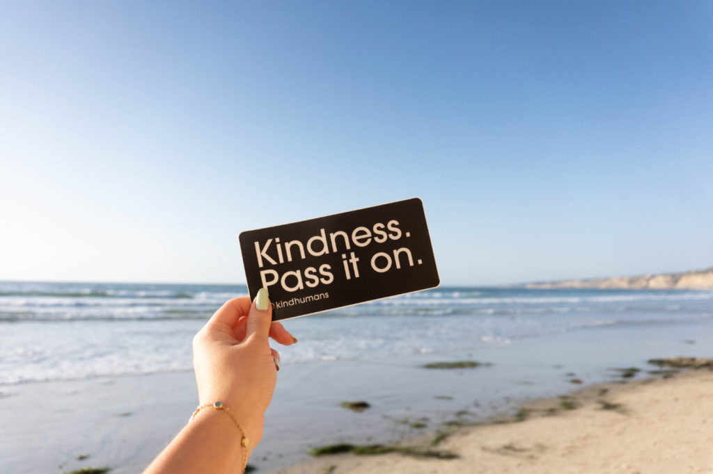 A person holding a sign that says: "Kindness. Pass it on."