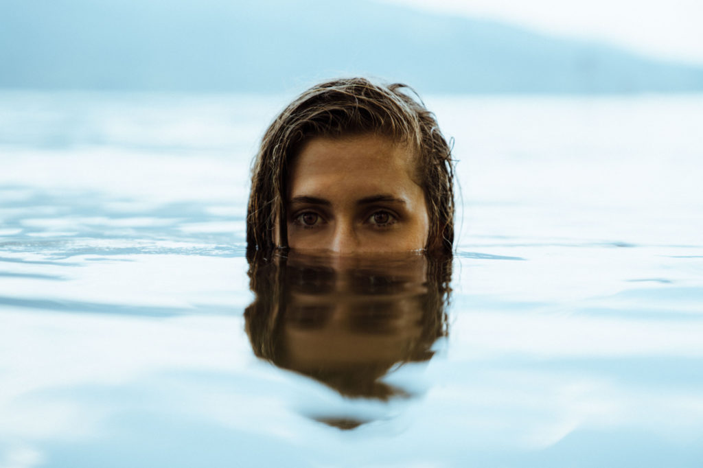 A woman submerged into water, with only a half of her head coming out.