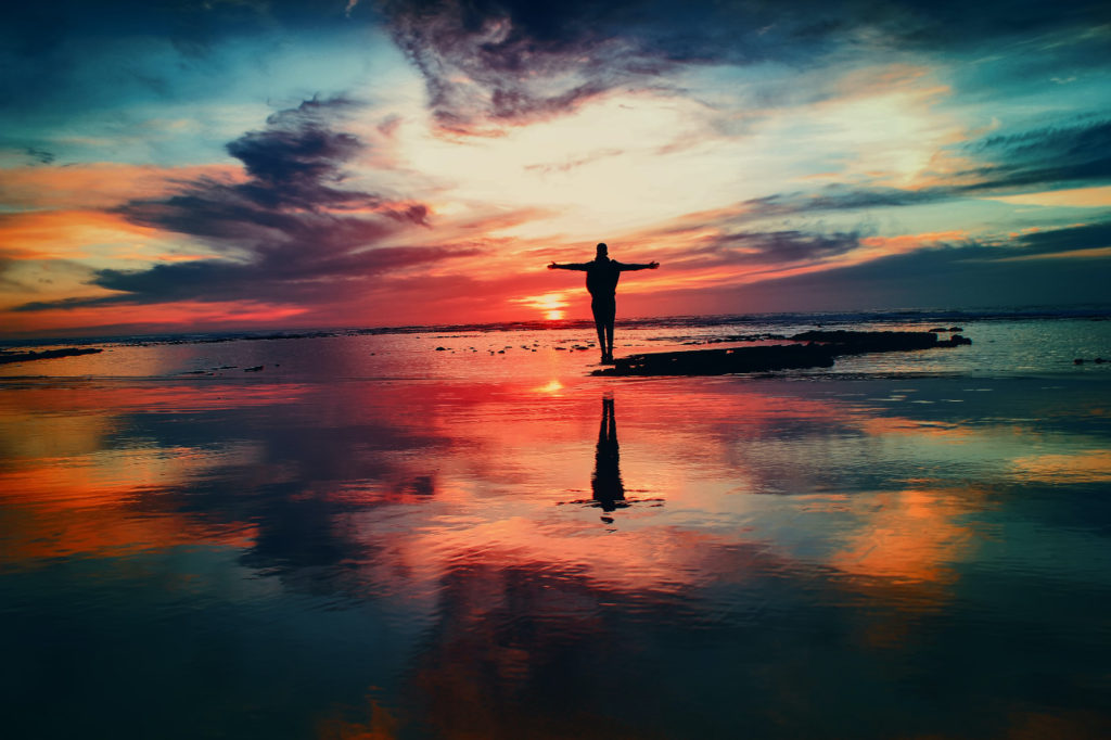 A person standing on a tiny island during a colorful sunset.