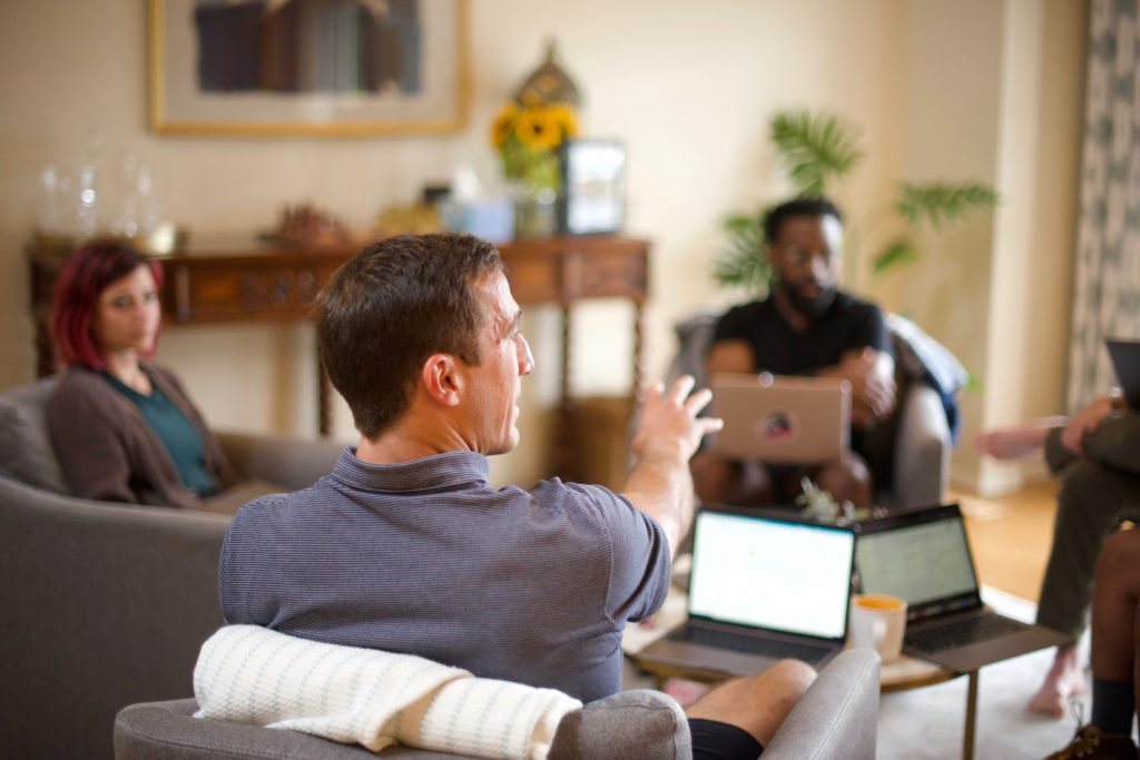 Three people in a discussion at a coffee table with opened laptops.
